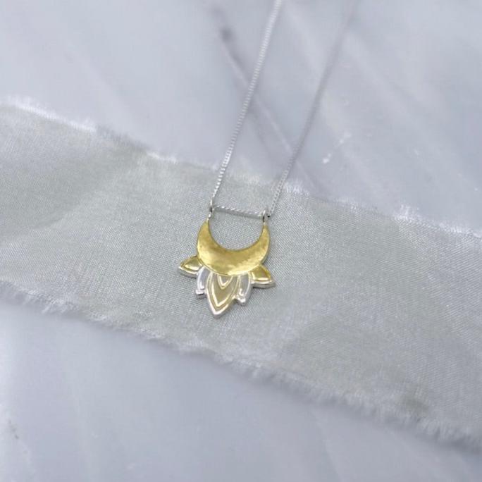 A sterling silver and gold necklace of moon and lotus flower design draped on a delicate piece of soft silk ribbon