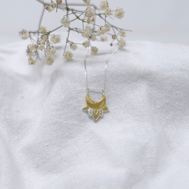 A piece of white linen with a sterling silver and gold crescent moon and lotus flower necklace on it