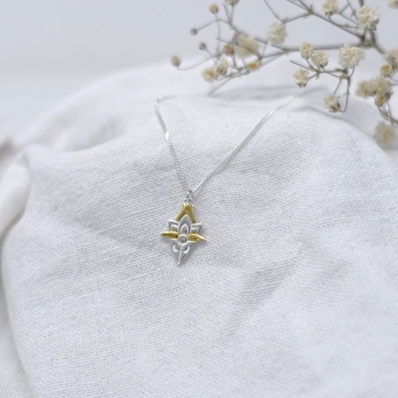 White linen cloth with a sterling silver and gold accent lotus flower and crescent moon necklace. 