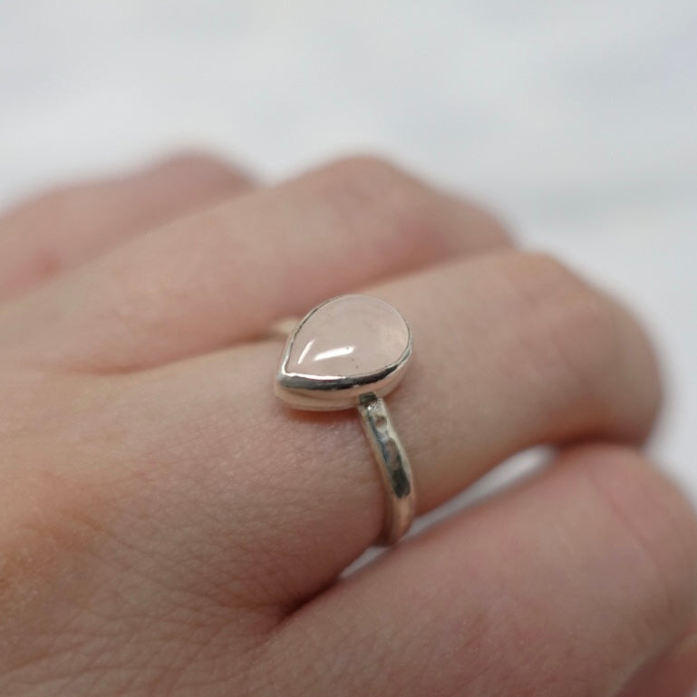 A models hand showing a pastel coloured rose quartz teardrop style ring